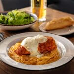 Plated Chicken Parmesan served with pasta, garnished with fresh basil and a sprinkle of grated Parmesan.