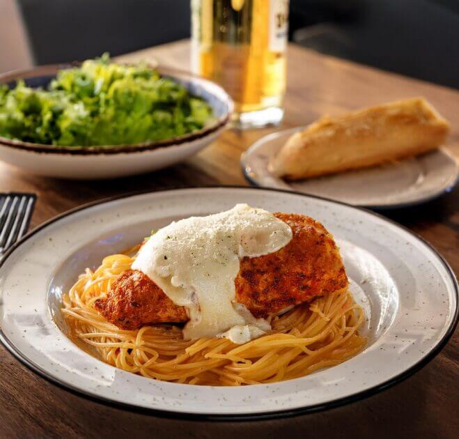 Plated Chicken Parmesan served with pasta, garnished with fresh basil and a sprinkle of grated Parmesan.