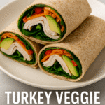 Close-up of three turkey veggie wraps in whole wheat tortillas on a white plate, filled with lean turkey slices, avocado, spinach, carrots, and red bell peppers, arranged neatly and cut to display the colorful, healthy ingredients.