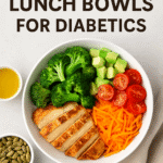 Grain-free diabetic lunch bowl featuring grilled chicken, broccoli, avocado, cherry tomatoes, and shredded carrots in a white bowl, served with pumpkin seeds and a small dish of dressing on a light background.